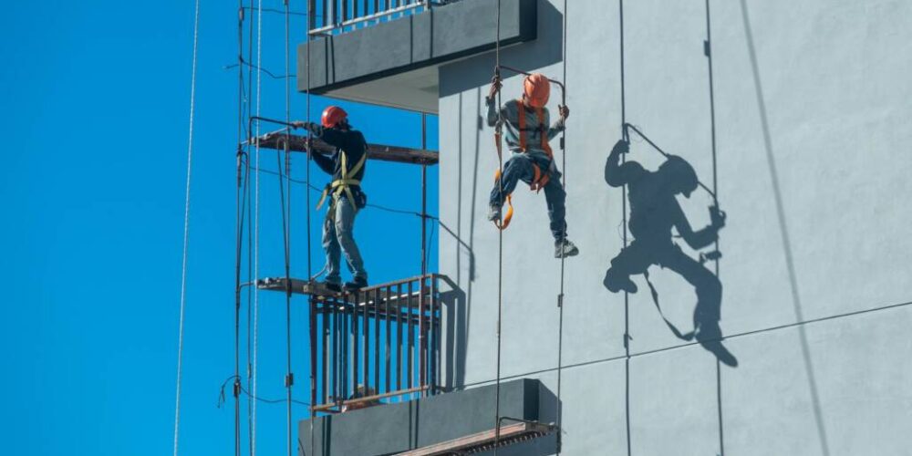 A couple of workers fixing and climbing a scaffolding while following all the safety measures